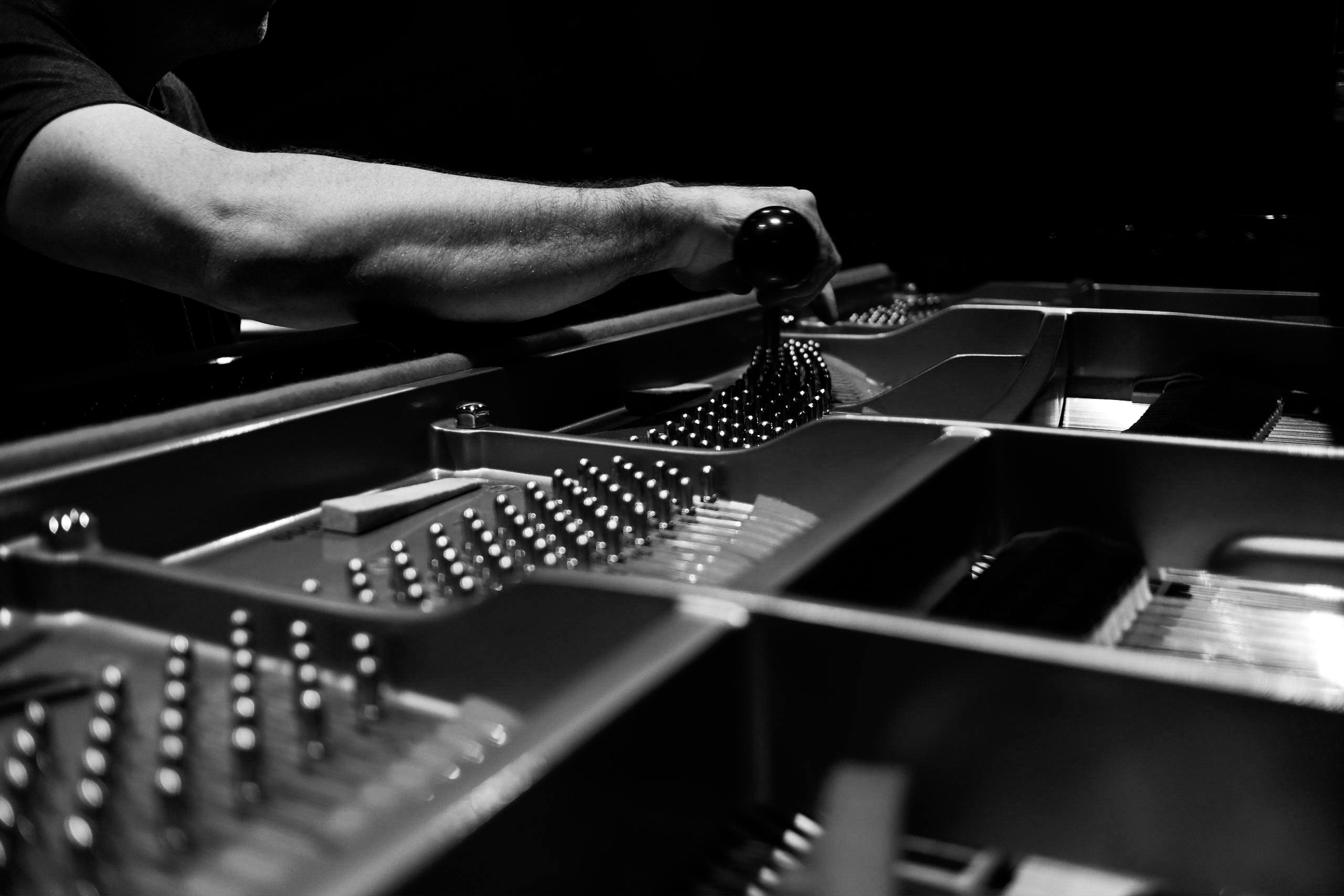 Black and white image of a piano tuner adjusting strings inside a grand piano, highlighting precision.