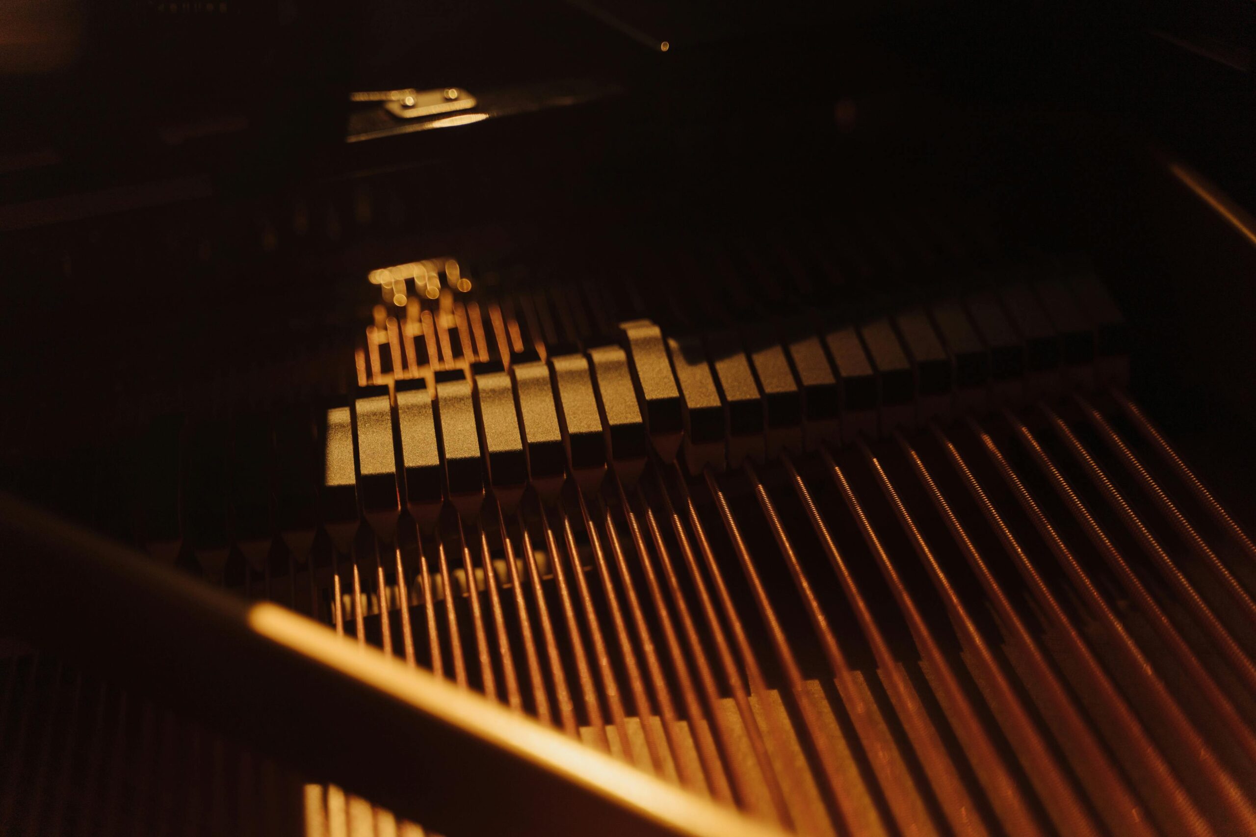Close-up image of piano strings and hammers under warm, intimate lighting within a grand piano.